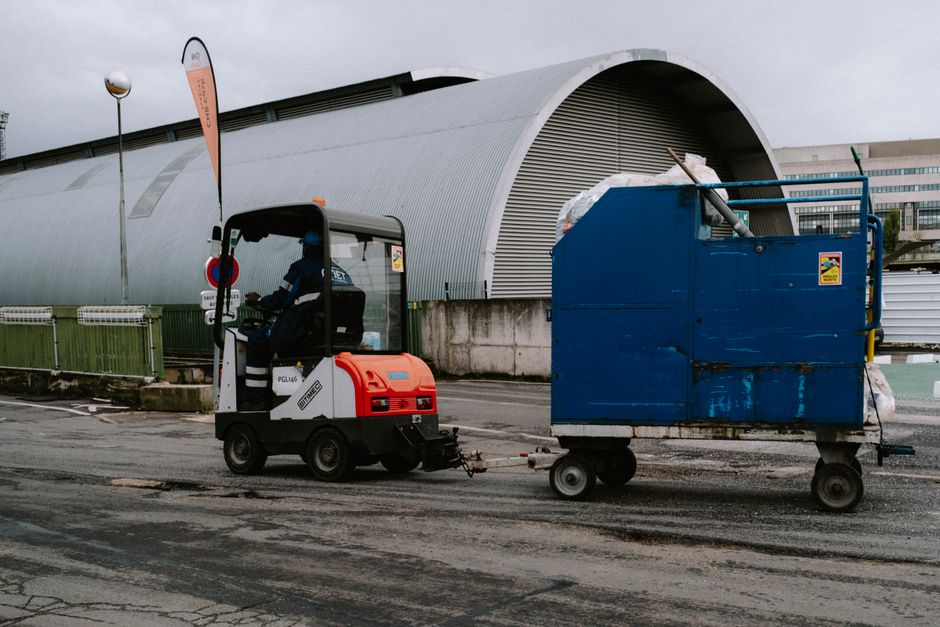 Forklift operator pulling a blue container outdoors near industrial facility.