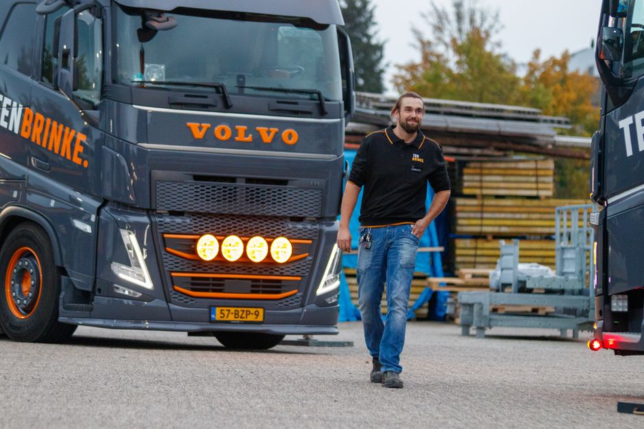 Truck driver walking near a Volvo truck in an industrial area during the day, showcasing logistics and transportation.